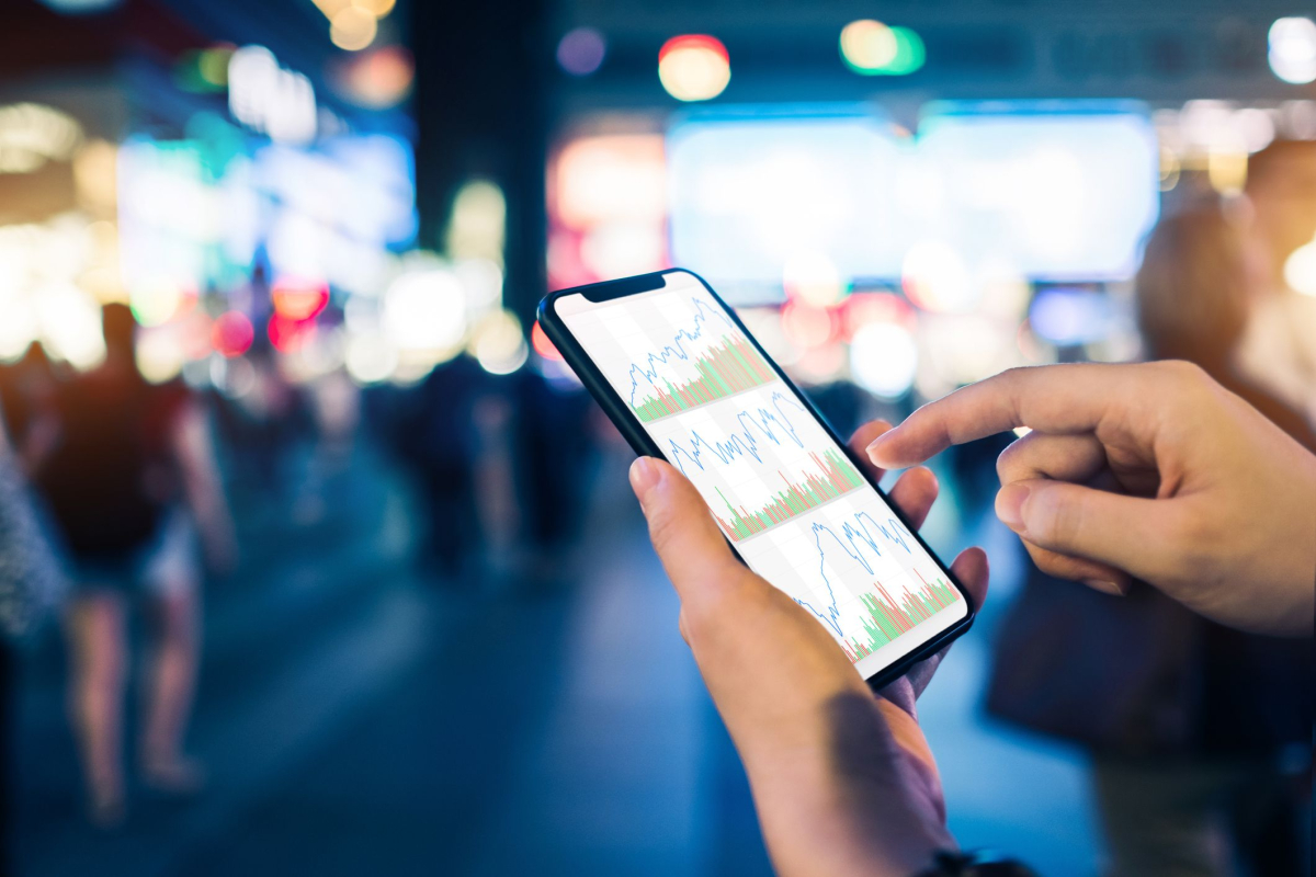 close up of human hands checking financial stock charts on smartphone in busy city street against neon commercial sign at night 994764592 aa617091531f4ff99f5521895ad1fd94