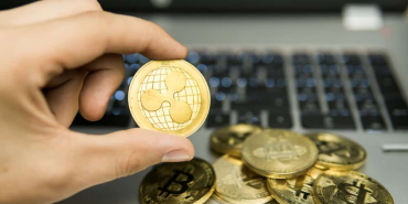 Male businessman hand holding Ripple coin on a background of laptop keyboard and pile of golden coins. Virtual money and Financial growth concept. Trading Mining of Ripples.